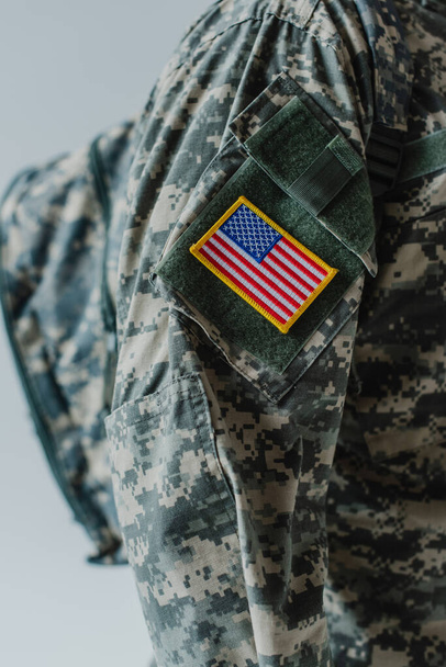 cropped view of American soldier in army uniform standing with backpack isolated on grey  - 写真・画像