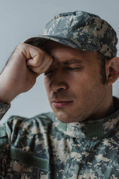 triste soldat en uniforme militaire pleurant les yeux fermés pendant la journée commémorative isolé sur gris  - Photo, image