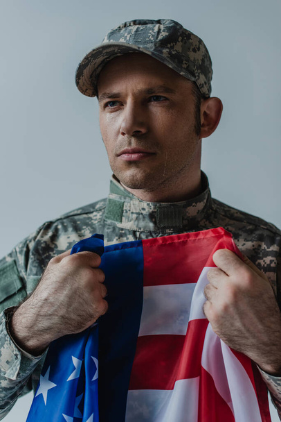 upset American soldier holding flag of United States while crying during memorial day isolated on grey  - Fotoğraf, Görsel