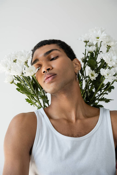 portré fiatal afro-amerikai srác fehér felső pózol fehér krizantém elszigetelt szürke - Fotó, kép