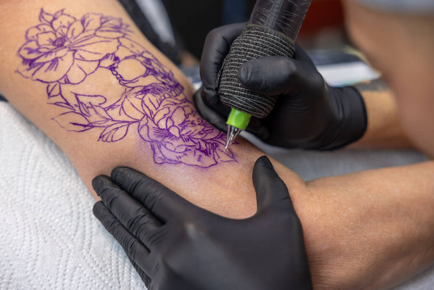 In the tattoo salon. Tattoo master drawing tattoo on womans arm - Foto, immagini