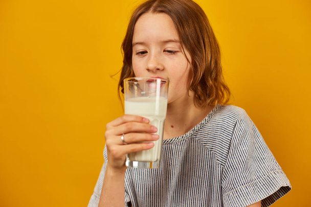 Pretty teen girl, child with a fresh glass of milk isolated on studio yellow background, strong bones, milk for growth, healthy lifestyle concept, copy space - Photo, Image