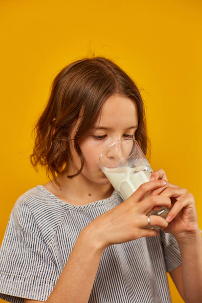 Mooie tiener meisje, kind met een vers glas melk geïsoleerd op studio gele achtergrond, sterke botten, melk voor de groei, gezonde levensstijl concept, kopieer ruimte - Foto, afbeelding