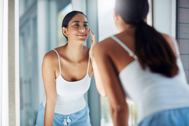 Mantener mi piel sana y húmeda. una atractiva joven que inspecciona su piel frente al espejo del baño - Foto, imagen