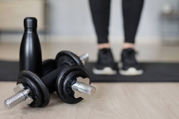 sport, training and fitness background - close up of black dumbbells and bottle of water, female legs on yoga mat - Foto, imagen