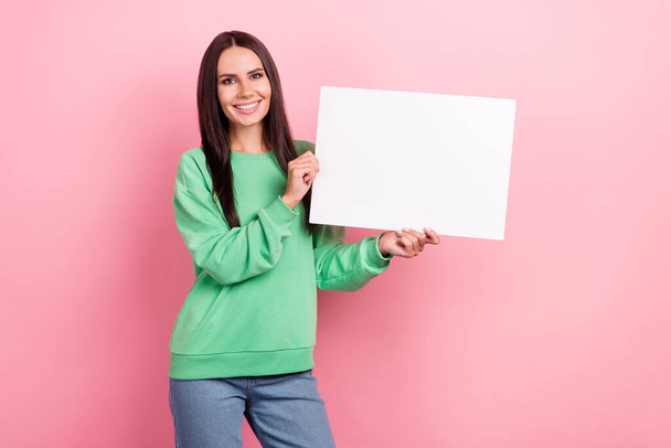 Photo of adorable youngster promo lady advertiser wear green sweatshirt hold paper placard empty space text isolated on pink color background. - Foto, Bild