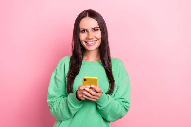 Photo of charming smiling good mood brunette hair lady wear green pullover hold phone review her new apple gadget isolated on pink color background. - Фото, изображение