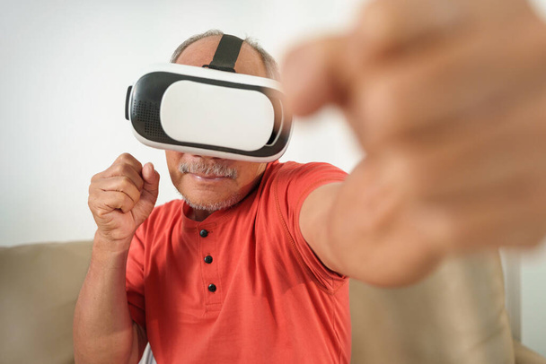 Asian Senior Adult Man is using VR glasses headset with virtual reality boxing game at home. - 写真・画像