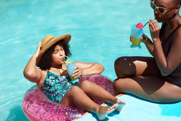Dos mujeres negras se relajan en la piscina, bebiendo un exquisito jugo de verano. Foto de alta calidad - Foto, imagen