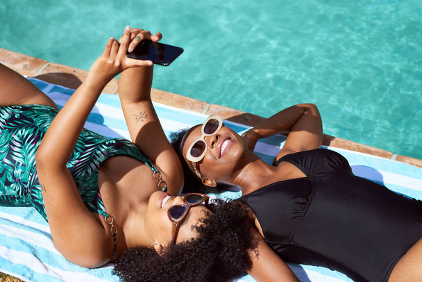 Kaksi ystävää uima-altaalla ottamassa selfieitä uimapuvuissa, kehonpositiivinen kesä. Laadukas kuva - Valokuva, kuva