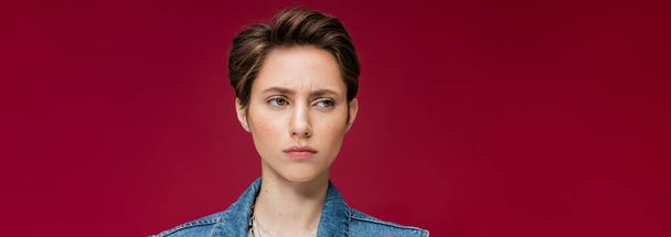 suspicious young woman with short hair looking away on burgundy background, banner  - Foto, Imagem