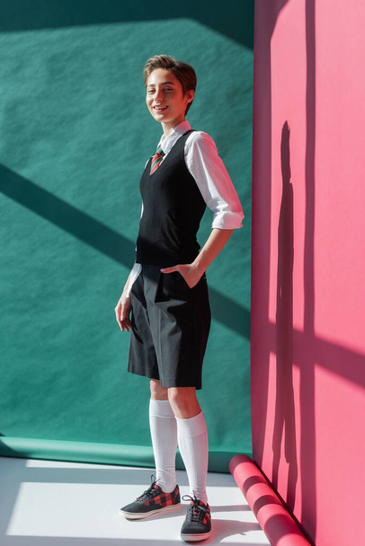 full length of happy young student with short hair posing with hand in pocket of black shorts on pink and green  - Foto, immagini