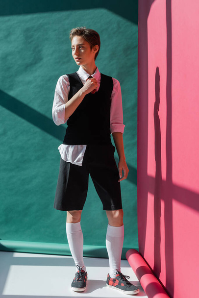 full length of stylish young woman with short hair posing in school uniform on pink and green  - Foto, Imagem