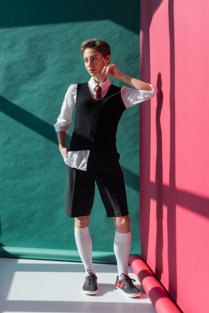 full length of young woman with short hair posing in school uniform on pink and green  - Foto, Imagem