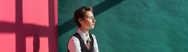 stylish young woman with short hair posing in school uniform on green and pink background with shadows, banner  - Foto, Imagen