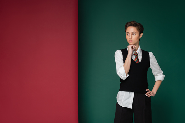 stylish young student with short hair posing with hand on hip on green and maroon background  - Photo, Image