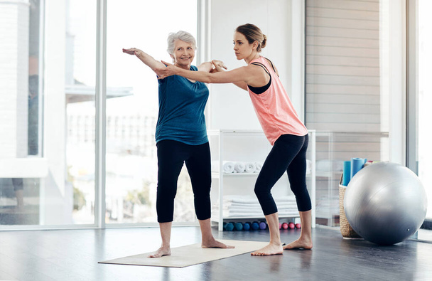 Yoga richtet sich an alle Altersgruppen. Fitnesstrainerin hilft einer Seniorin bei einem Yoga-Kurs - Foto, Bild