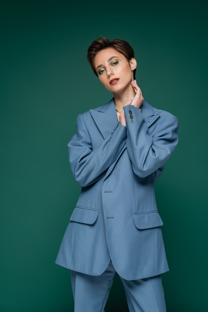 young woman with short hair posing in blue suit on turquoise green background  - Foto, Bild