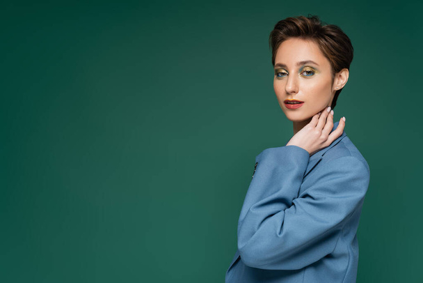 charming young woman with short hair posing in blue suit on turquoise green background  - Photo, image