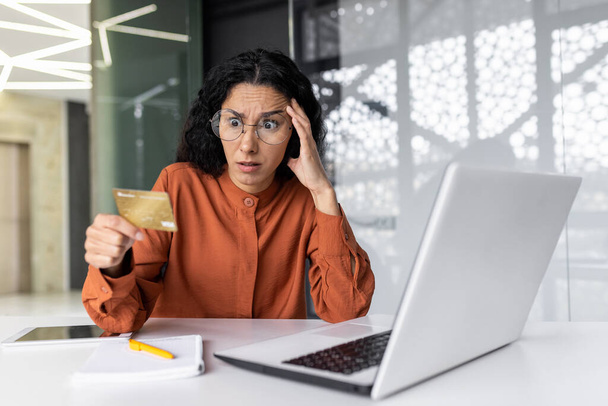 Dissatisfied and angry businesswoman inside the office, hispanic woman at workplace cheated by online fraudsters, female employee trying to transfer money from bank credit card, received error. - Foto, Imagem