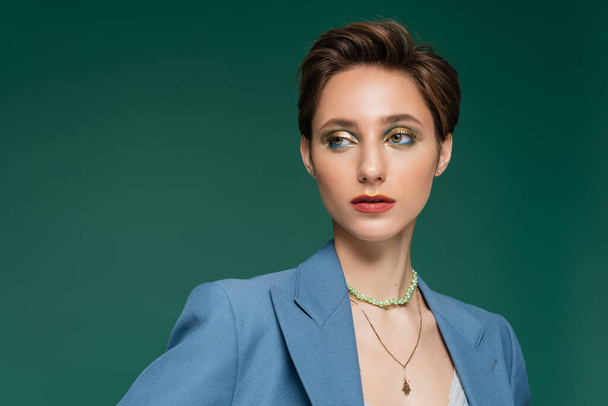 elegant young woman with short hair and bright makeup looking away isolated on turquoise  - Foto, immagini