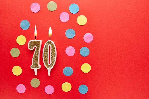 Number 70 on a red background with colored confetti. Happy birthday candles. The concept of celebrating a birthday, anniversary, important date, holiday. Copy space. banner - Foto, Imagem