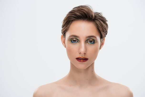 young woman with short hair and bright makeup standing with bare shoulders isolated on grey  - Foto, imagen