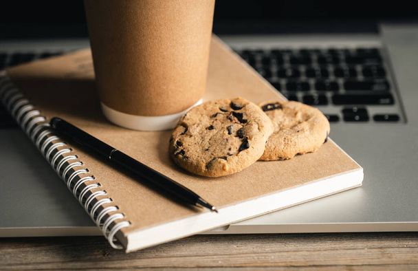 Trendy Office Concept, craft Paper Cup, cookies and recycled notebook on Laptop Keyboard. - Foto, imagen
