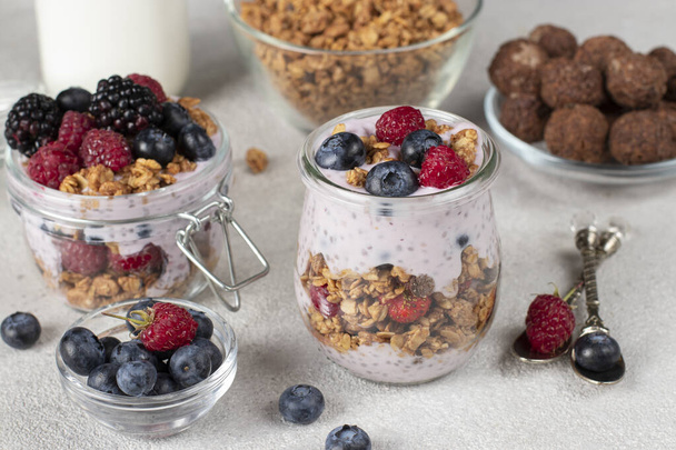 Chocolate granola with berries, chia seeds and natural yogurt in two jars on light gray background - Fotografie, Obrázek