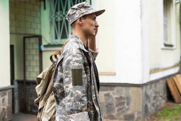 Photo of soldier in camouflaged uniform holding olive colored backpack. - Foto, imagen