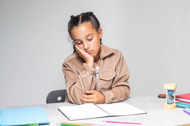 Досить маленька дівчинка втомилася робити домашнє завдання за столом
 - Фото, зображення