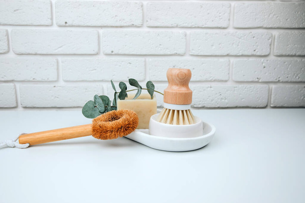 Set of eco friendly products. Washing brush and natural soap on a white marble tray with eucalyptus sprigs. Front view - Foto, Imagen
