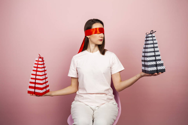 A cute blindfolded brunette with a stack of beautiful gifts in two hands, choosing which one. A girl with gift boxes or presents, and ribbons in her hands. - Foto, Bild