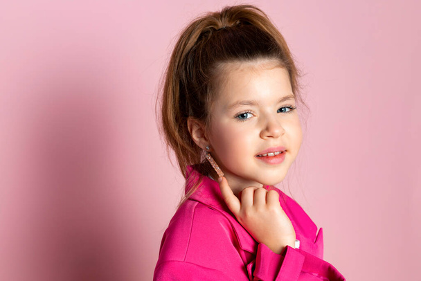Πορτρέτο ενός μικρού κοριτσιού με ένα τεράστιο ροζ σακάκι. Παιδί που φοράει ρούχα ενηλίκων. Απομονωμένα σε ροζ φόντο. - Φωτογραφία, εικόνα