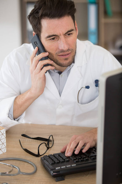 male doctor using mobile phone in clinic against computer - Photo, image