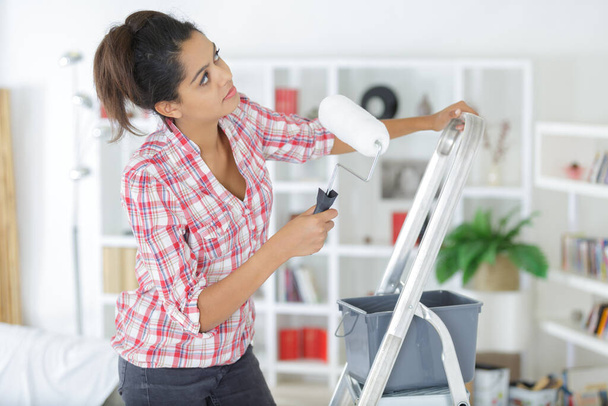 young woman with paint roller doing renovation at new house - Foto, Bild