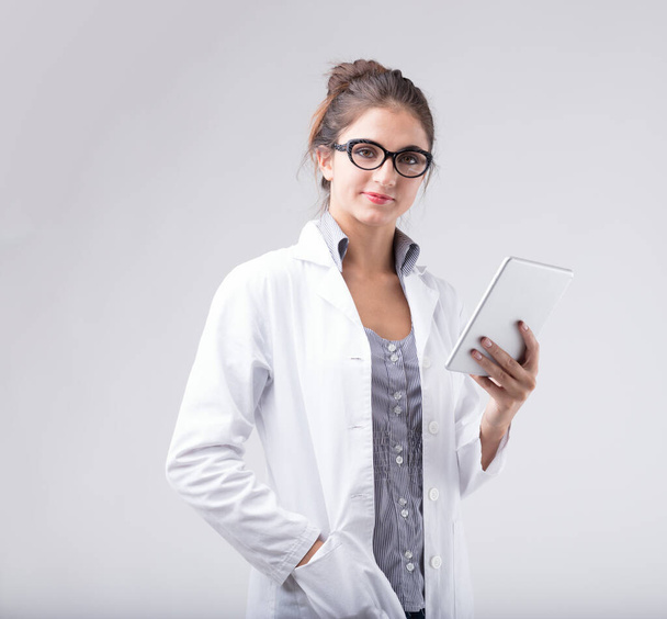 Женщина в белом халате и очках держит цифровой планшет и смотрит прямо на зрителя. Она профессионал медицинской науки, специалист по технологиям или аналитик по данным? Она биолог? - Фото, изображение