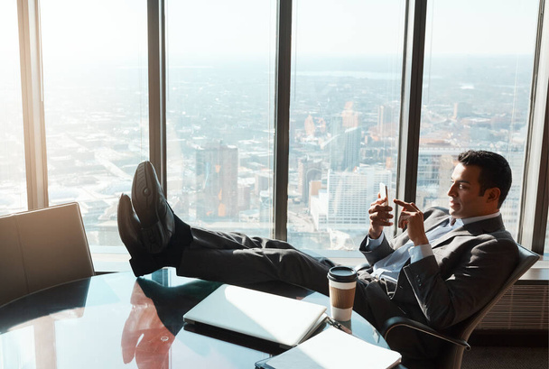 Сядьте и посмотрите, как я добьюсь успеха. молодой бизнесмен, пользующийся мобильным телефоном, расслабляясь, стоя ногами на столе в офисе - Фото, изображение