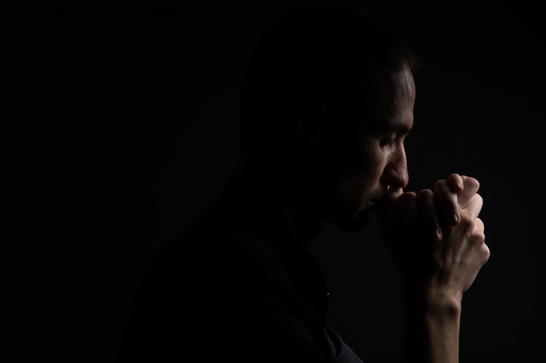 Close up of faithful mature man praying, hands folded in worship to god with head down and eyes closed in religious fervor. Black background. Concept for religion, faith, prayer and spirituality. - Foto, Imagen