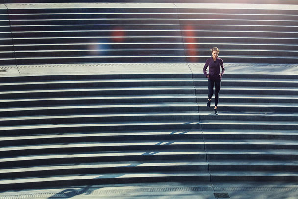 Keep it moving. High angle shot of an attractive young sportswoman running up and down stairs outside - Foto, afbeelding