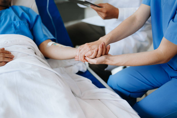 Female doctor holding male patient hand on the bed with receiving saline solution in hospital or clinic - Photo, image