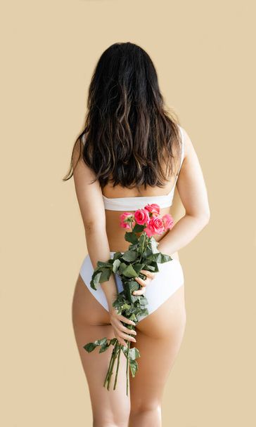 sexy asian girl in white lingerie holding a pink rose against beige background - Photo, Image