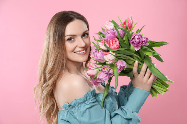 Happy young woman with bouquet of beautiful tulips on pink background - Fotó, kép