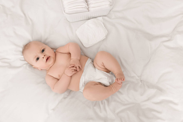 Cute baby and diapers on white bed, top view - Φωτογραφία, εικόνα
