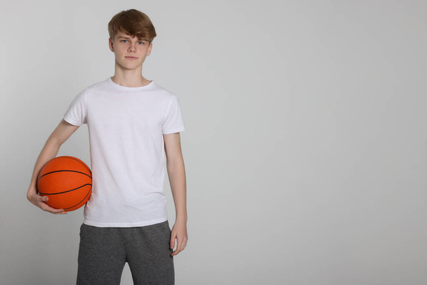 Teenage boy with basketball ball on light grey background. Space for text - Фото, изображение