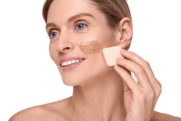 Woman applying foundation on face with makeup sponge against white background - Zdjęcie, obraz