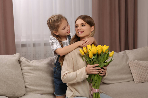 Córeczka gratuluje mamie bukietu żółtych tulipanów w domu. Szczęśliwego Dnia Matki - Zdjęcie, obraz