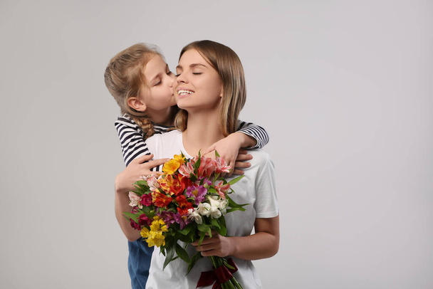 Little daughter congratulating her mom with flowers on white background. Happy Mother's Day - Photo, image