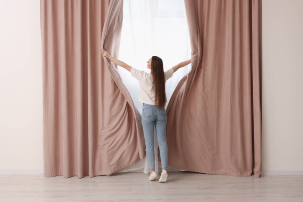 Woman opening stylish curtains at home, back view - Φωτογραφία, εικόνα