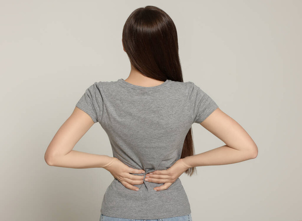 Woman suffering from back pain on light grey background. Arthritis symptoms - Фото, зображення